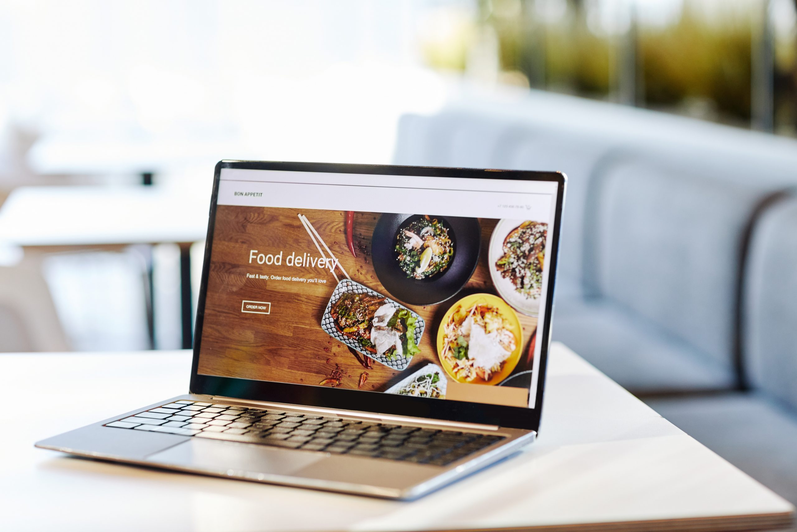 Background image of opened laptop with Food delivery website on table in food court or cafe interior, copy space